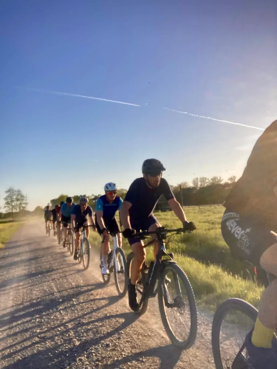 Een rij fietsers volgt een gravelpad langs het veld in de avondzon.