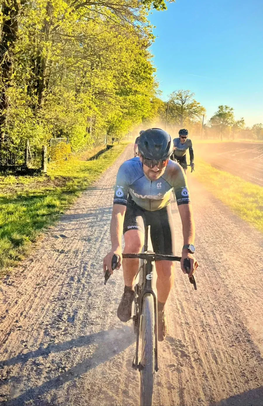 Een fietser in clubkleding rijdt over een zonnig gravelpad.