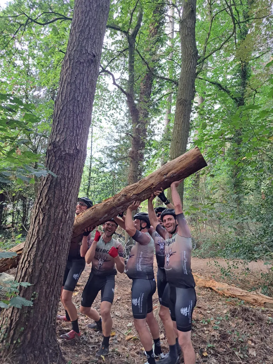 Clubleden tillen samen een boomstam op tijdens een stop in het bos.