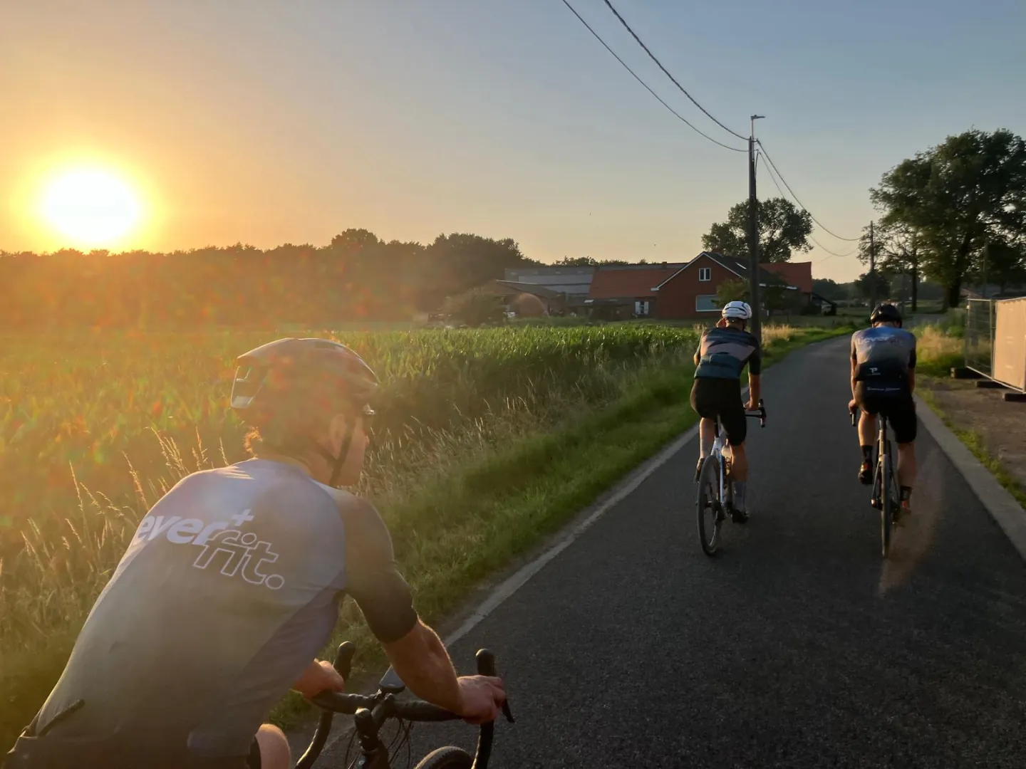 Clubleden fietsen langs velden bij zonsondergang.